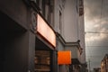 Empty orange square shop signboard hanging on a building facade, visible against a cloudy sky in a European city street, ideal for Royalty Free Stock Photo