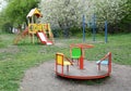 Empty outdoor playground for children with a slide, carousel, pull up, chin up bar in the park with blooming trees in the Royalty Free Stock Photo