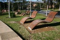 Empty outdoor wood slat chaise lounge chairs hovering above grass in park at University of Sydney, Australia