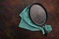 Empty oval cast iron frying pan and linen towel. Rusty dark background. Top view with copy space. Flat lay