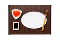 Empty oval white plate with chopsticks for sushi, ginger and soy sauce on dark bamboo mat background. Top view with copy space for Royalty Free Stock Photo