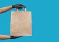 Empty paper bag. Shopping bag for groceries. Hands in black gloves. On a blue background Royalty Free Stock Photo