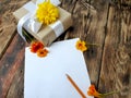 Empty paper blank with gift and flowers on wooden background.
