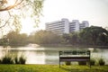 An empty park bench in the garden with lake view and apartment in the city park at morning with sunbeam. green tree and beautiful Royalty Free Stock Photo