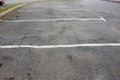 An empty parking lot features multiple cracked asphalt surfaces by trees roots