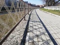 Empty paved river embankment with shadow from fence.