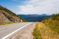 Empty paved road and gravel shoulder against hills and mountains