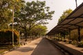 Empty paved road lined with green trees and a long covered pedestrian walkway structure under a sunny sky. Royalty Free Stock Photo