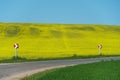 An empty paved road passes by a field with flowering rapeseed. Winding road and road signs. Haystacks on the horizon in the field Royalty Free Stock Photo