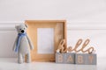 Empty photo frame, cute toy bear and decor near wall, space for text. Baby room interior element Royalty Free Stock Photo