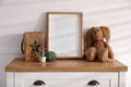Empty photo frame near cute toy bunny and decor on dresser, space for text. Baby room interior element Royalty Free Stock Photo