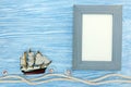 Empty photo frame, rope and ship on blue wooden background Royalty Free Stock Photo