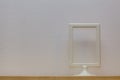 An empty photo frame stands on a wooden shelf against a background of white wallpaper. Royalty Free Stock Photo