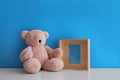 Empty photo frame and teddy bear on white table near light blue wall. Space for design Royalty Free Stock Photo