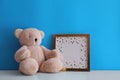 Empty photo frame and teddy bear on white table near light blue wall. Space for design Royalty Free Stock Photo