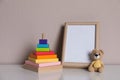 Empty photo frame, toy bear and pyramid on white table near grey wall. Space for design Royalty Free Stock Photo