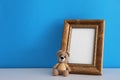 Empty photo frame and toy bear on white table near light blue wall. Space for design Royalty Free Stock Photo