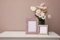 Empty photo frames and beautiful bouquet on white table near pink wall, space for text Royalty Free Stock Photo