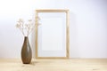 Empty picture frame mockup and a brown ceramic vase with filigree gypsophila on a wooden table against a light gray wall, minimal Royalty Free Stock Photo