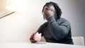 Empty piggy bank. Sad african american man putting one coin inside. Small savings Royalty Free Stock Photo