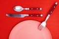 Empty pink plate, red Spoon, fork, and knife, on a red background, top view. Space for text Royalty Free Stock Photo