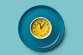 Empty plate with alarm clock on blue background, intermittent fasting concept. Royalty Free Stock Photo