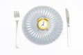 Empty plate with alarm clock, fork and knife on a white background, intermittent fasting concept. Royalty Free Stock Photo