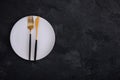 Empty plate with fork and knife on dark stone background. Gold and black tableware with white plate Royalty Free Stock Photo