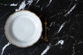 Empty plate with golden fork on dark granite background with copy space, top view