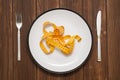 Empty plate with measure tape, knife and fork on the wooden background. Diet food concept top view Royalty Free Stock Photo