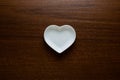 Empty plate in the shape of a heart on a wooden table in the center of the frame. Ceramic glossy dishes on a dark nutty background