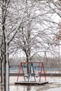 Empty playground, bright swing set for children covered with snow on winter background, no people. Cold frosty weather, abandoned Royalty Free Stock Photo