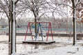 Empty playground, bright swing set for children covered with snow on winter background, no people. Cold frosty weather, abandoned Royalty Free Stock Photo