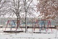 Empty playground, bright swing set for children covered with snow on winter background, no people. Cold frosty weather, abandoned Royalty Free Stock Photo