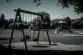 empty playground with swings and slides in the foreground, and a view of a picturesque park in the background Royalty Free Stock Photo