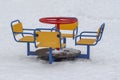 Empty playground in winter, cold weather, low temperature, swing yellow red blue metal multicolored funny mini carousel. white