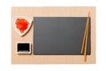 Empty rectangular black slate plate with chopsticks for sushi, ginger and soy sauce on brown sushi mat background. Top view with Royalty Free Stock Photo