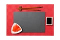 Empty rectangular black slate plate with chopsticks for sushi, ginger and soy sauce on red mat sushi background. Top view with Royalty Free Stock Photo