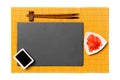 Empty rectangular black slate plate with chopsticks for sushi, ginger and soy sauce on yellow bamboo mat background. Top view with Royalty Free Stock Photo