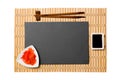 Empty rectangular black slate plate with chopsticks for sushi, ginger and soy sauce on yellow bamboo mat background. Top view with Royalty Free Stock Photo