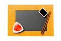 Empty rectangular black slate plate with chopsticks for sushi, ginger and soy sauce on yellow bamboo mat background. Top view with Royalty Free Stock Photo