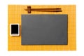 Empty rectangular black slate plate with chopsticks for sushi and soy sauce on yellow bamboo mat background. Top view with copy Royalty Free Stock Photo