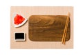 Empty rectangular brown wooden plate with chopsticks for sushi, ginger and soy sauce on brown sushi mat background. Top view with Royalty Free Stock Photo
