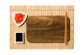 Empty rectangular brown wooden plate with chopsticks for sushi, ginger and soy sauce on yellow bamboo mat background. Top view Royalty Free Stock Photo