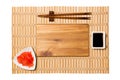 Empty rectangular brown wooden plate with chopsticks for sushi, ginger and soy sauce on yellow bamboo mat background. Top view Royalty Free Stock Photo