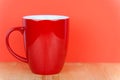an empty red ceramic coffee mug with a handle stands on a natural wooden board in front of a colored background Royalty Free Stock Photo