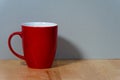 an empty red ceramic coffee mug with a handle stands on a natural wooden board in front of a colored background Royalty Free Stock Photo
