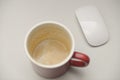 Empty red coffee mug with espresso foam residue on white desk beside wireless computer mouse minimalist workspace view Royalty Free Stock Photo