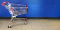 Empty red shopping cart parked on blue wall background for customer take it to carry stuff or merchandise in supermarket