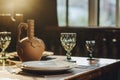 Empty reserved table in restaurant with clay vase for wine, drinking glass and plates